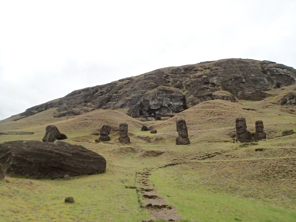 The ancient moai quarry Rano Raraku with scattered moai, some half buried in the ground, some only partly carved our in the rock wall.